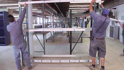 Two employees install pallet rack section.