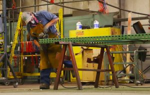 Employee wears proper PPE equipment while grinding a pallet rack upright.