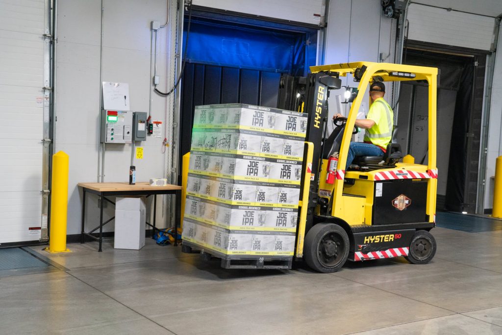 Forklift operator drives a loaded pallet through loading dock area.