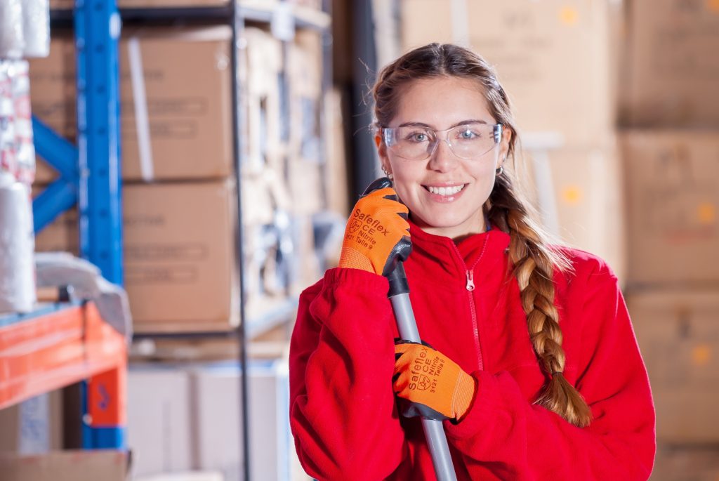 Warehouse employee with a broom smiles at camera.