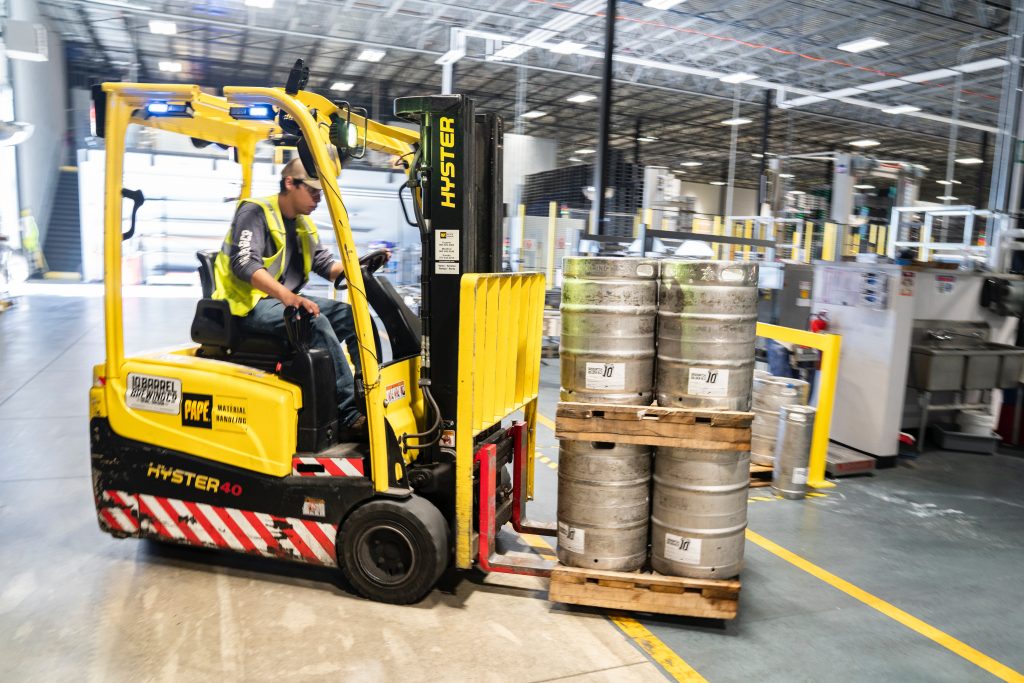 Forklift operator lifts a load of containers stacked on pallets.