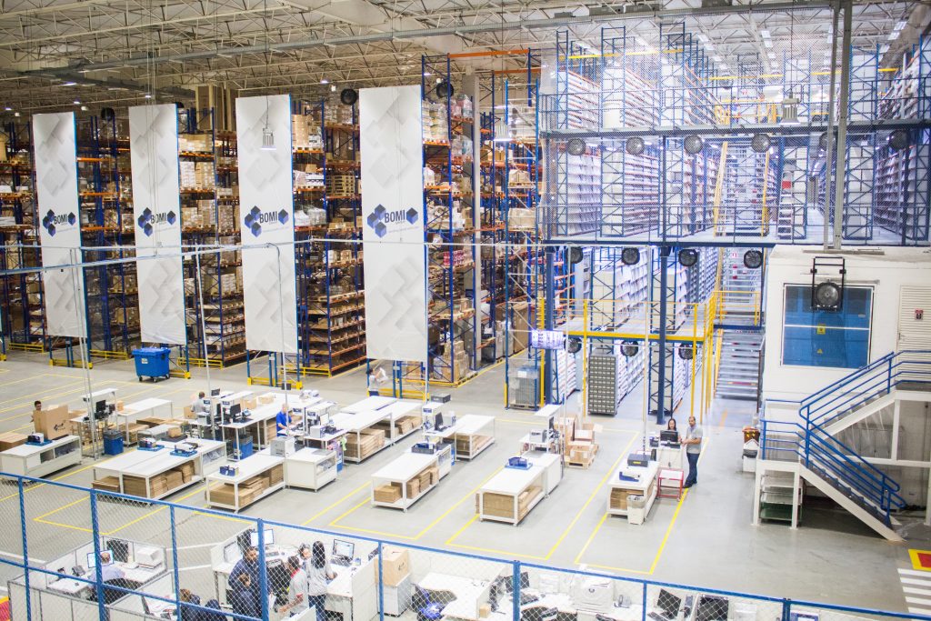 Interior warehouse with employees at work tables with pallet rack and mezzanine systems.