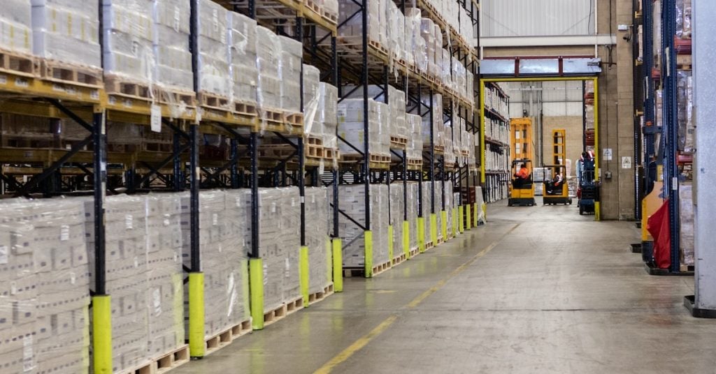 Warehouse aisle with pallet rack on side and forklifts