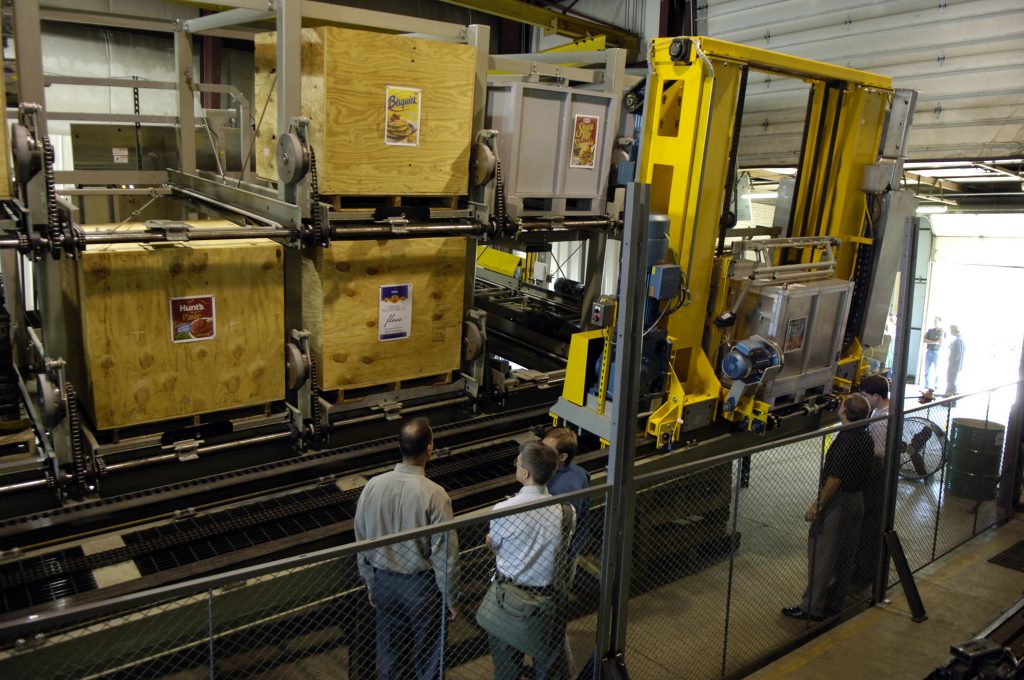 An ASRS set up in a warehouse; workers are in the warehouse and wooden boxes are located within the system