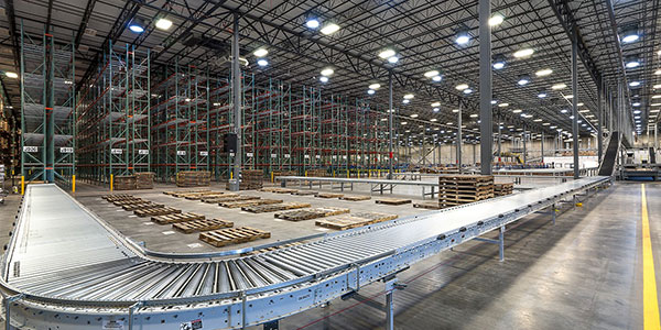 Interior of a large warehouse with a pallet racking system behind a conveyor system.