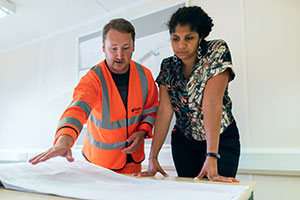 Two employees discuss warehouse layout over a blueprint