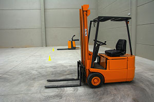 Orange and black forklift sitting in an empty warehouse.