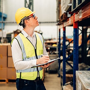 A worker uses a clipboard to check the maintenance of a pallet rack.