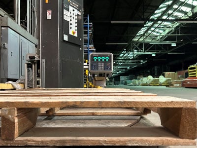 Empty wooden pallet sitting on a scale in a warehouse.