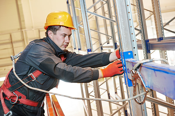 Man in safety gear assembling material handling equipment in a warehouse, showcasing safe and efficient installation practices.