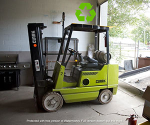 Used green forklift in a garage with a recycling symbol above it