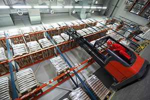 A worker uses a forklift to place like-items together on a pallet rack.