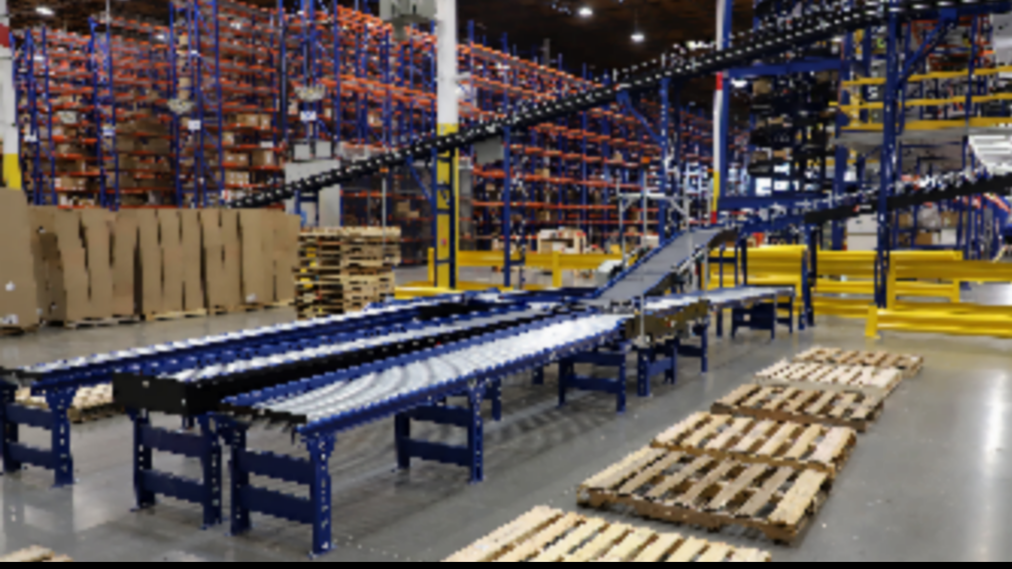Automated conveyor in a warehouse with pallet rack system in the background