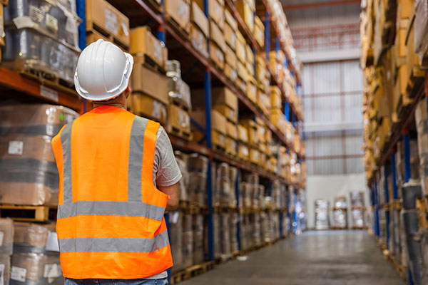 Warehouse manager looks down a pallet rack aisle